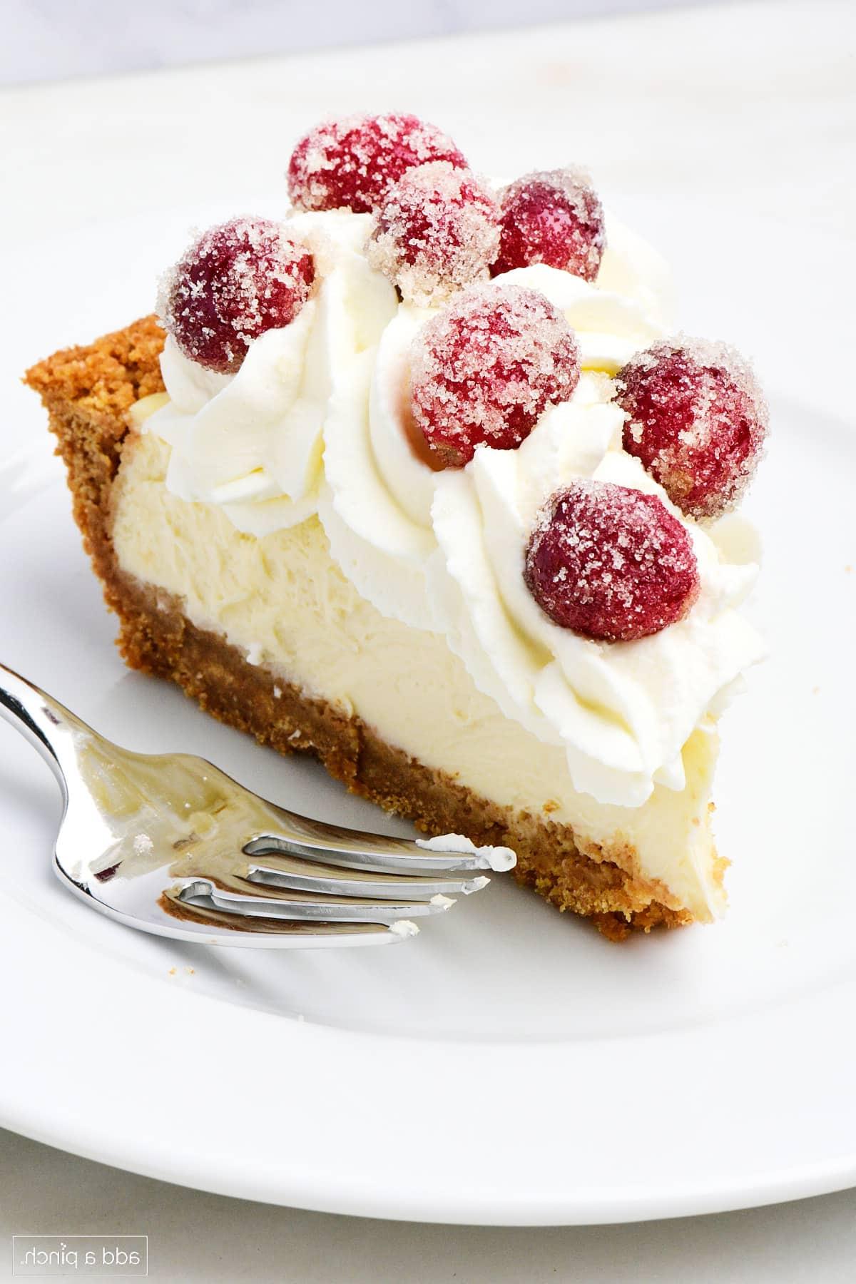 Συνταγή για Εύκολη Τάρτα Τσιζκέικ 2 Μια φέτα cheesecake pie με σαντιγί και ζαχαρωμένα cranberries σε λευκό πιάτο.