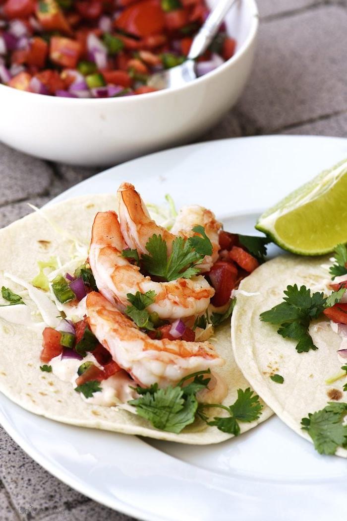 Συνταγή Τάκος Γαρίδας 3 Tacos με γαρίδες σε πιάτο με μια φέτα λάιμ, δίπλα σε ένα μπολ με φρέσκο pico de gallo.