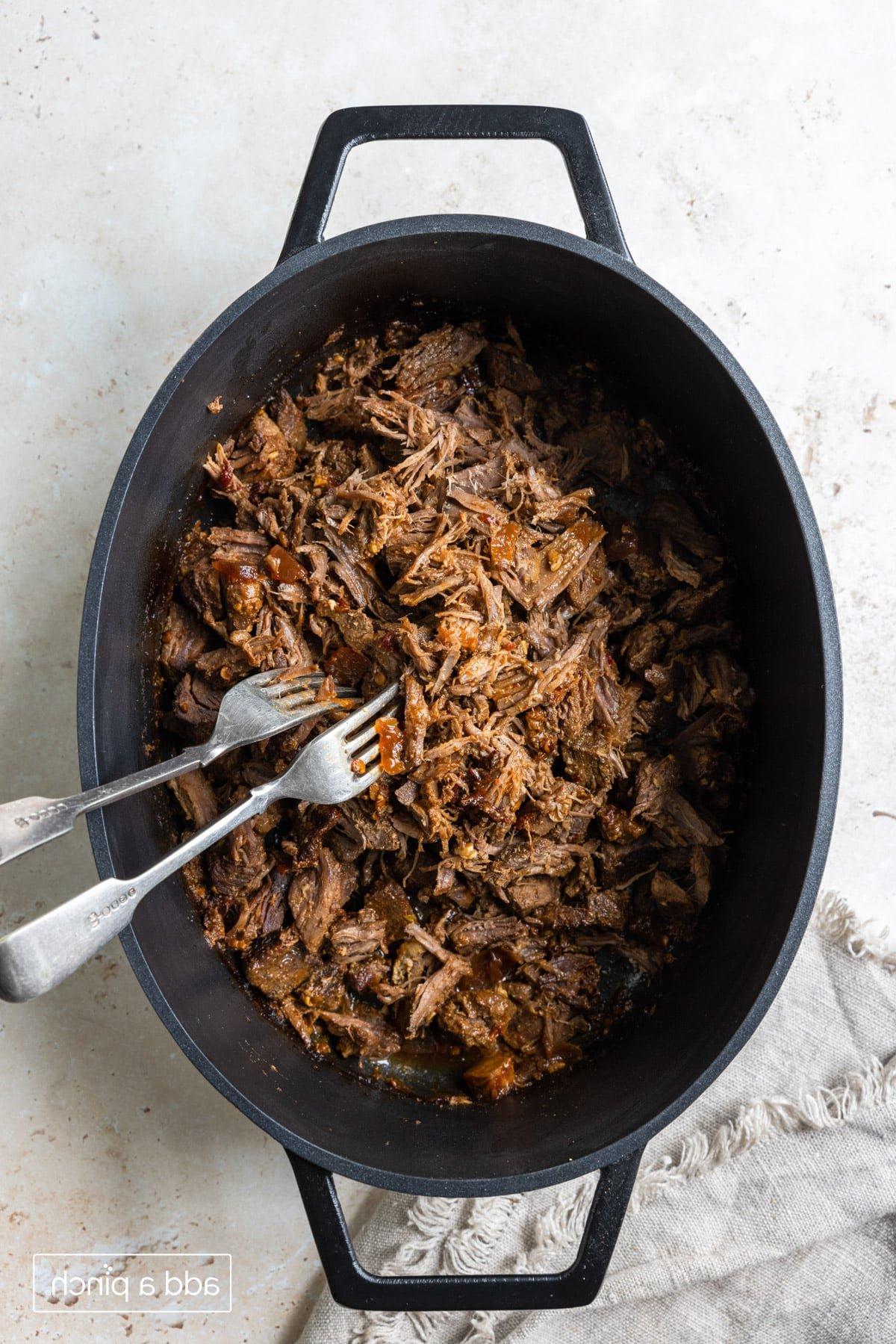 Φωτογραφία από Barbacoa μοσχαριού τεμαχισμένο σε μια κατσαρόλα με δύο πιρούνια.