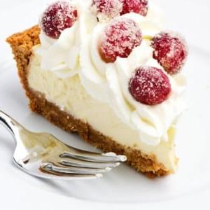 Συνταγή για Εύκολη Τάρτα Τσιζκέικ 9 Μια φέτα cheesecake pie με σαντιγί και ζαχαρωμένα cranberries σε λευκό πιάτο.