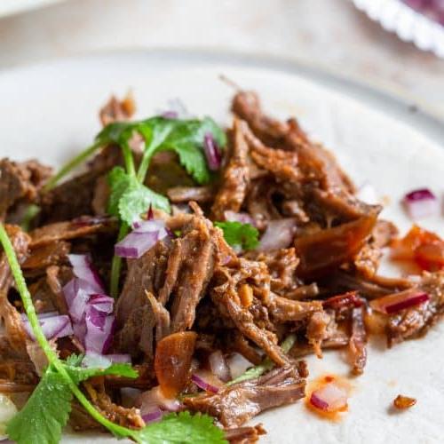 Φωτογραφία από Barbacoa σε μαλακή τορτίγια με κόλιανδρο, κόκκινο κρεμμύδι και επιπλέον σάλτσα περιχυμένη από πάνω.