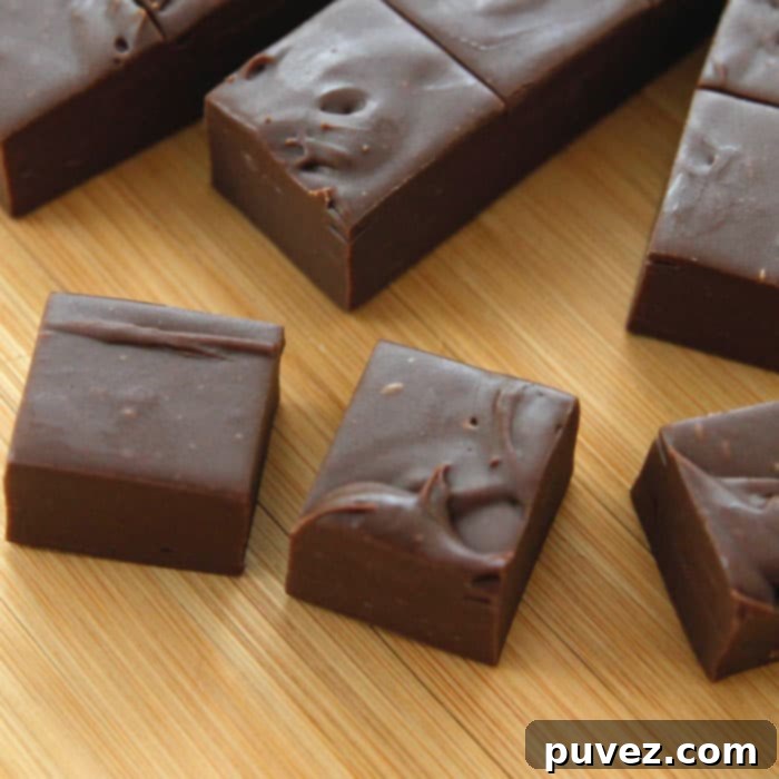 A large slab of 3-minute fudge on a wooden board, showcasing its smooth texture and rich color, with some squares already cut.
