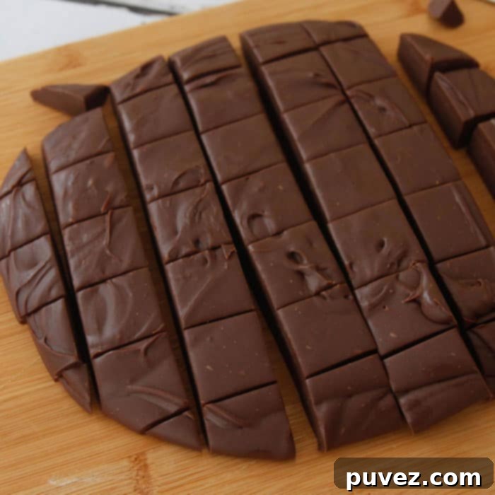 A round slab of three minute fudge, perfectly cut into uniform squares, rests on a rustic wooden board, ready to be enjoyed.
