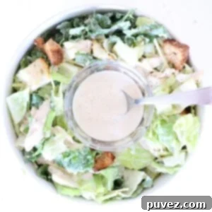 One bowl of Caesar salad with a small glass bowl of Caesar dressing with a spoon in the center.