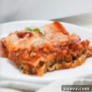 One serving of lasagna on a white plate with a napkin in front of the plate.
