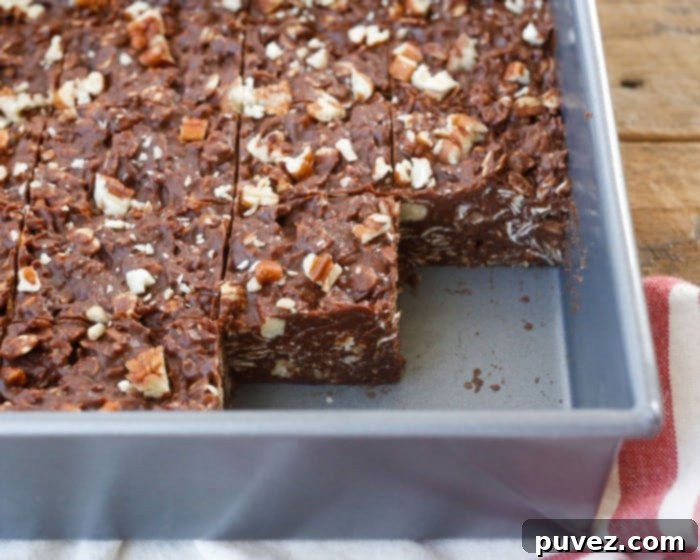Close-up of a stack of Coconut Pecan No-Bake Chocolate Bars, showing the texture of coconut, pecans, and oats embedded in chocolate.