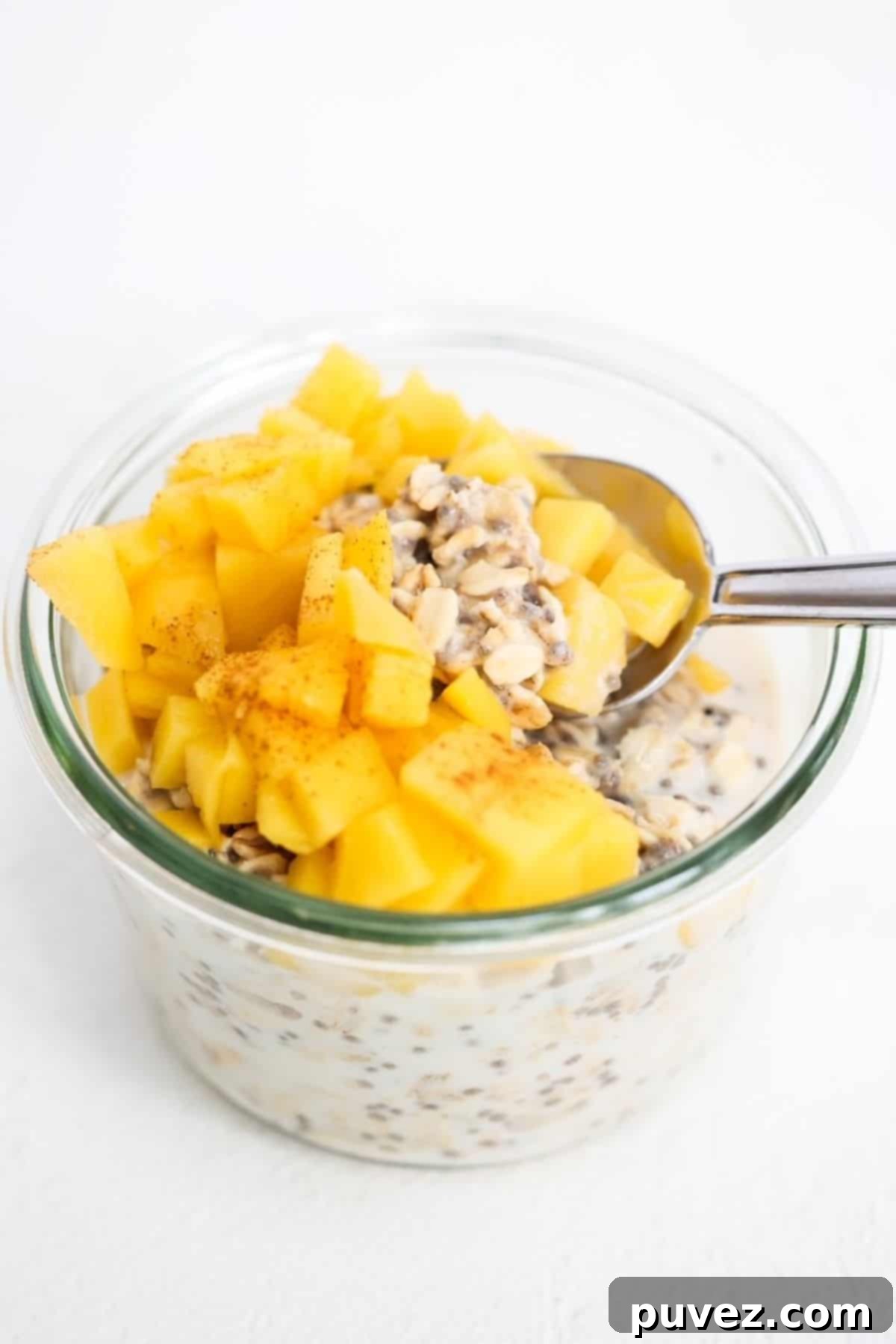 Mango overnight oats in a glass jar with a spoon, ready for breakfast.