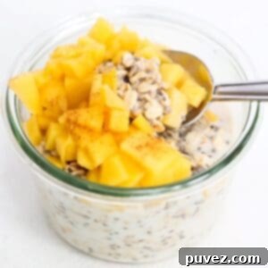 Overnight oats topped with pieces of fresh mango and a spoon.