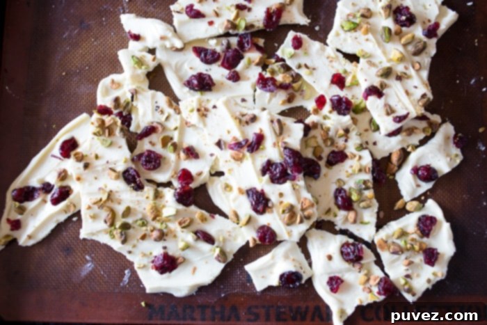 Close-up of freshly made White Chocolate Cranberry Pistachio Bark on a baking sheet, showcasing the scattered toppings before breaking.
