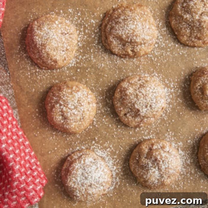 A batch of Toffee Pecan Snowdrop Cookies cooling on a wire rack after being baked, with a final dusting of confectioners' sugar for a classic snowdrop appearance.