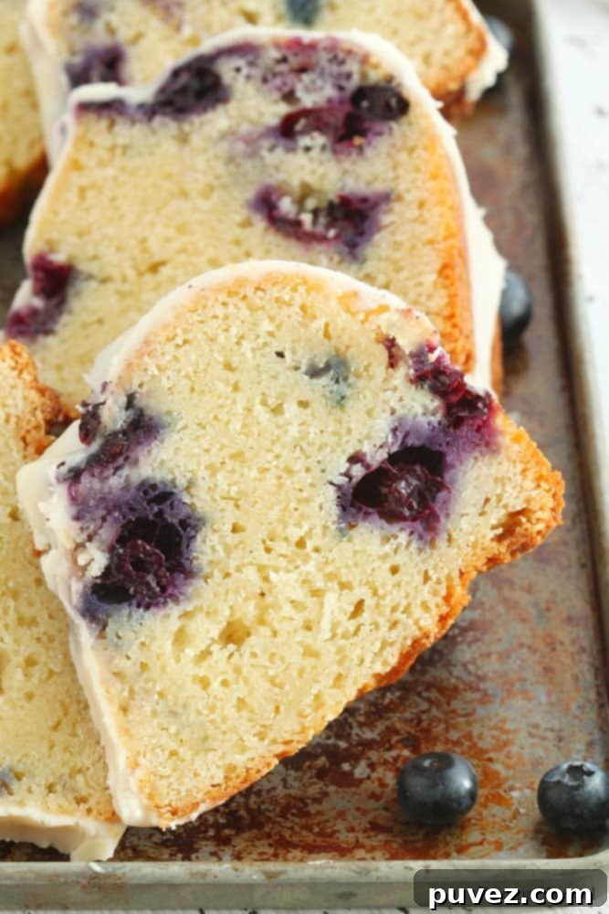A slice of blueberry bundt cake on a white plate, showcasing its moist crumb and blueberries