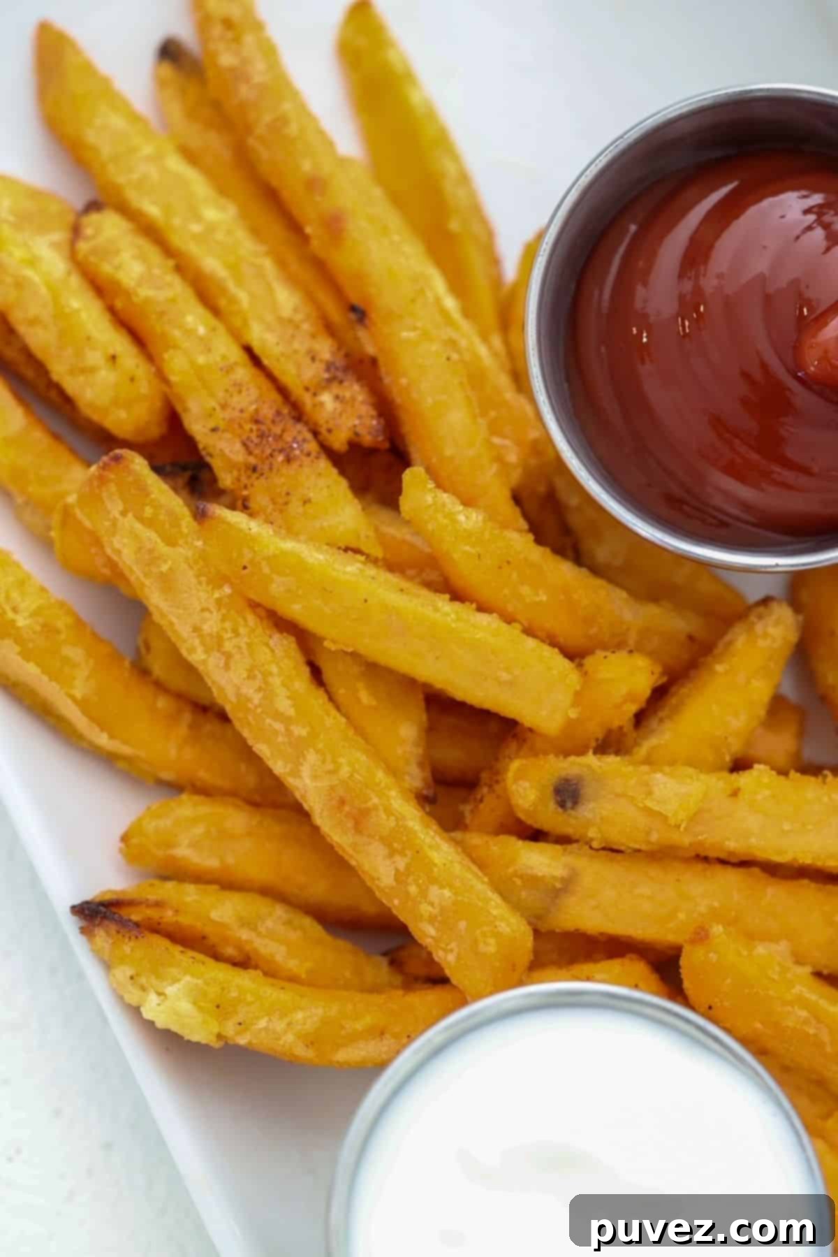 Crispy sweet potato fries served on a white plate with ketchup and Greek yogurt dip in small condiment cups.