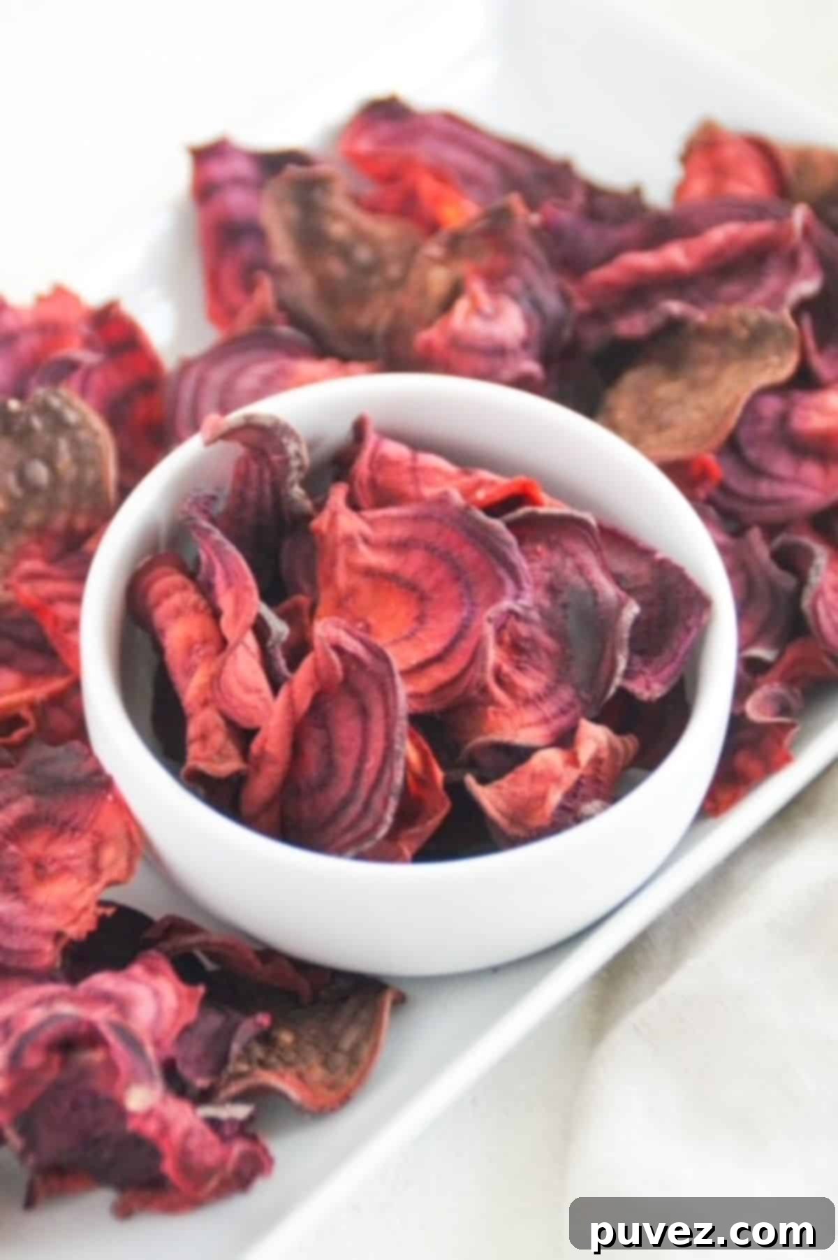 Perfectly crispy beet chips in a white bowl, with a side of more beet chips on a white serving dish, ready to be enjoyed.