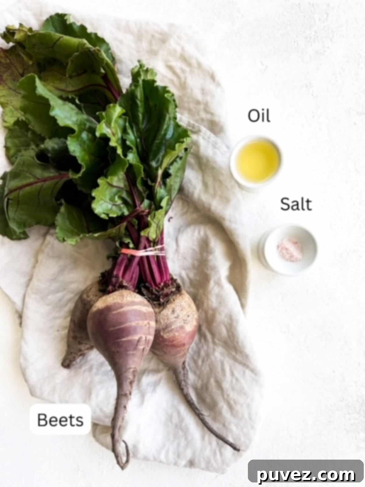 One vibrant bunch of fresh beets on a linen napkin, accompanied by a bottle of olive oil and a salt shaker, highlighting the simple ingredients.