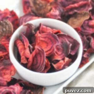 Delicious and crispy air fryer beet chips served in a white bowl, with more chips artfully arranged on a white platter, inviting to snack.