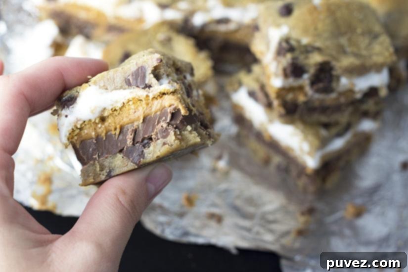 Hands spreading softened marshmallow fluff on cookie s'mores bars