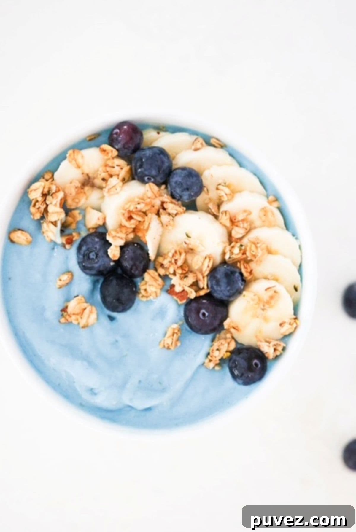 Blue smoothie bowl topped with banana slices, blueberries, and granola.