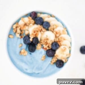 Blue smoothie bowl topped with sliced banana, blueberries, and granola.