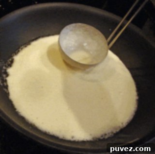 Image showing thin crepe batter being spread in a hot pan.