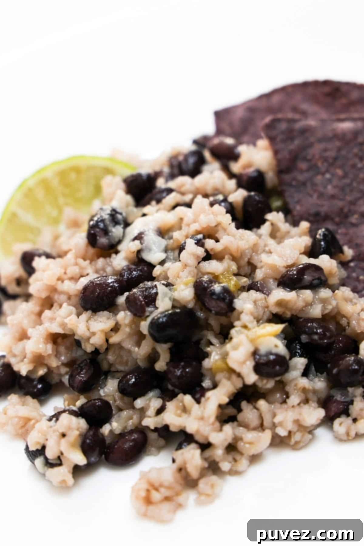 Black beans and rice with a lime wedge and a few blue tortilla chips on a white plate.