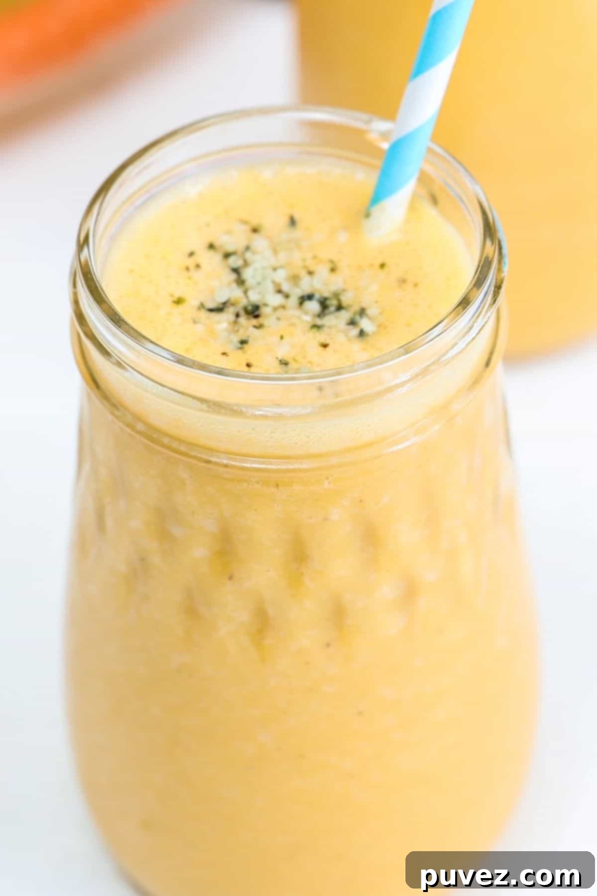 Carrot banana smoothie in a glass jar with a blue and white striped straw.