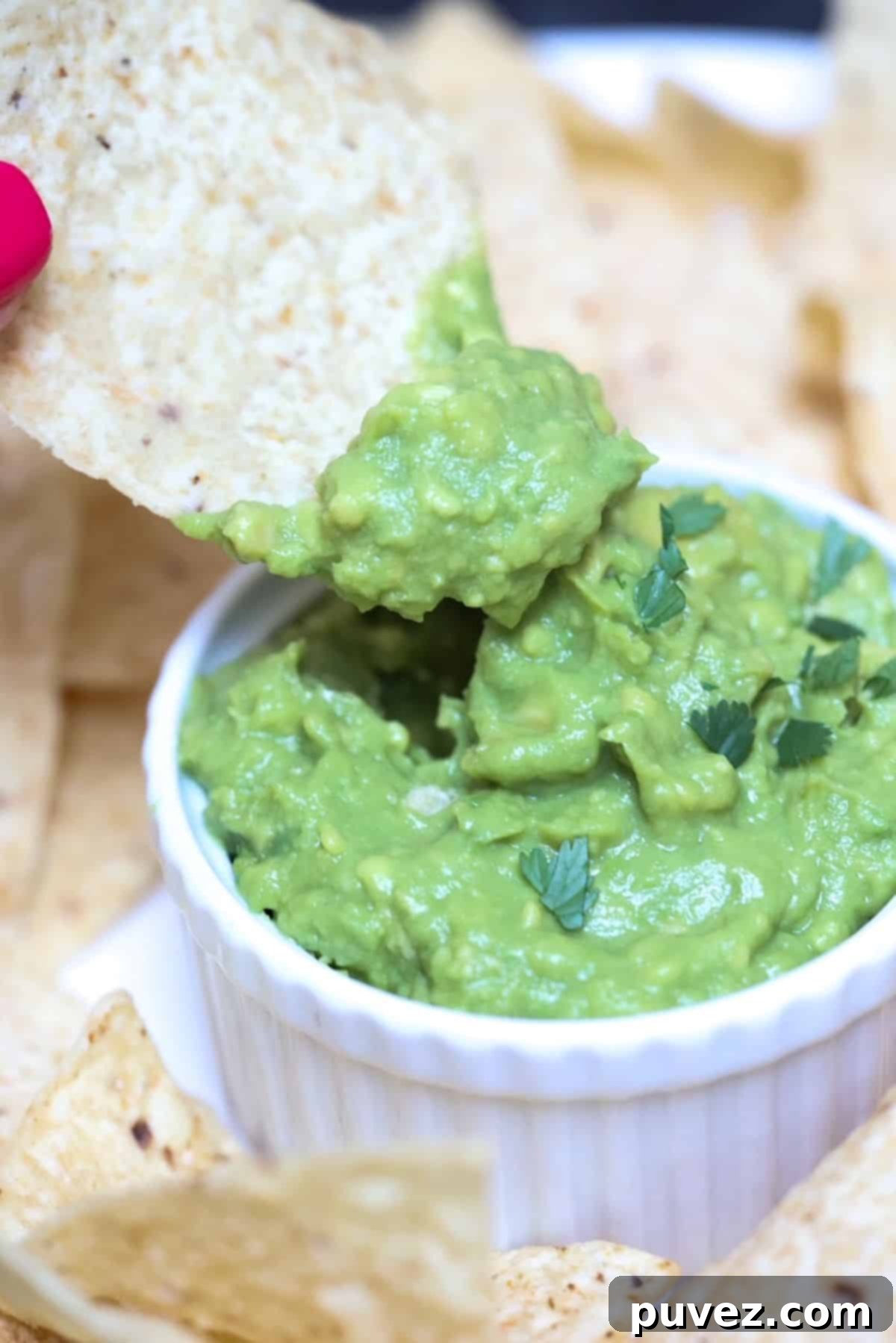 A chip dipped in fresh, homemade 4-ingredient guacamole served in a white ramekin, highlighting its creamy texture.