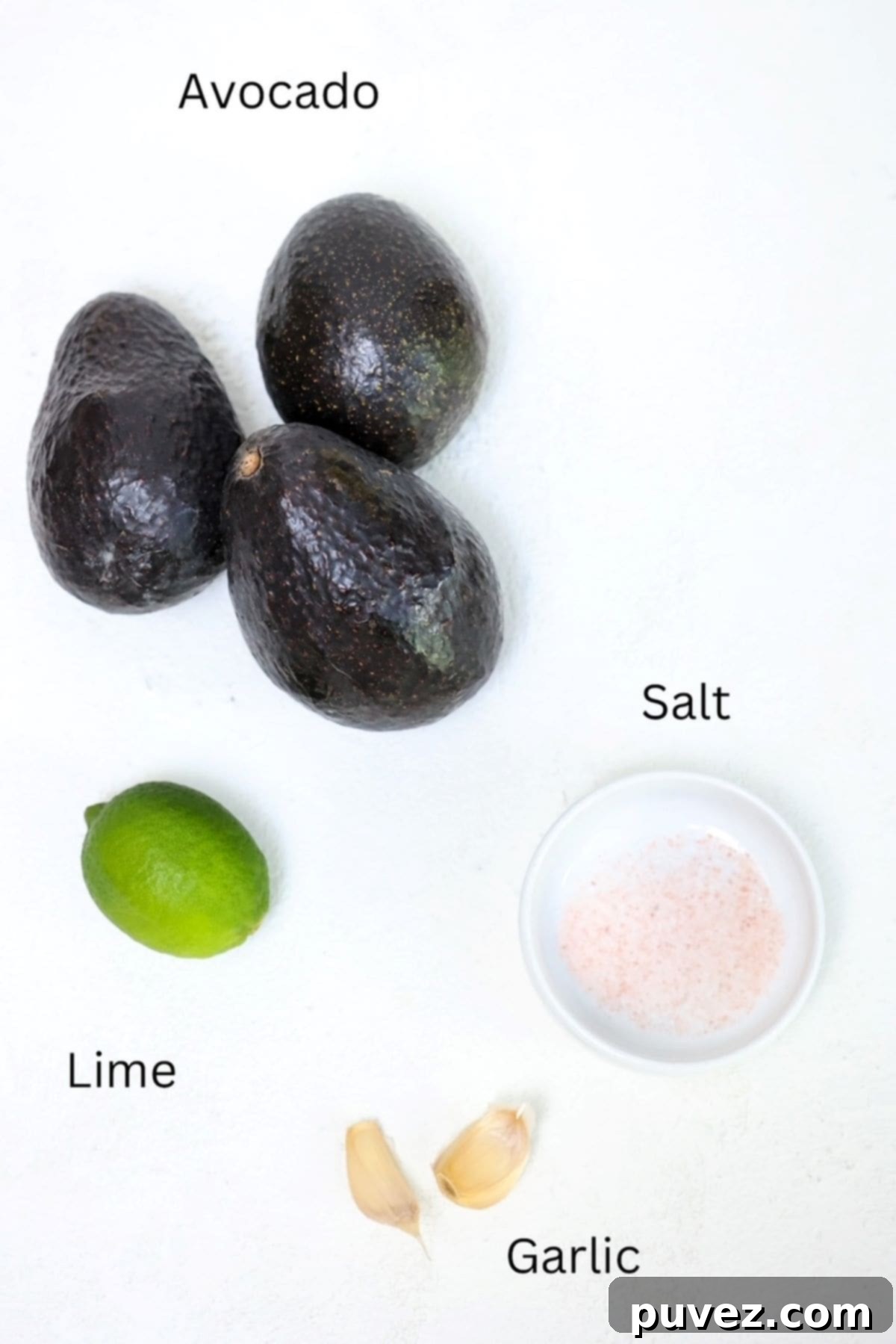 Four ingredients for easy guacamole: avocado, lime, garlic, and salt, clearly labeled on a rustic wooden board.