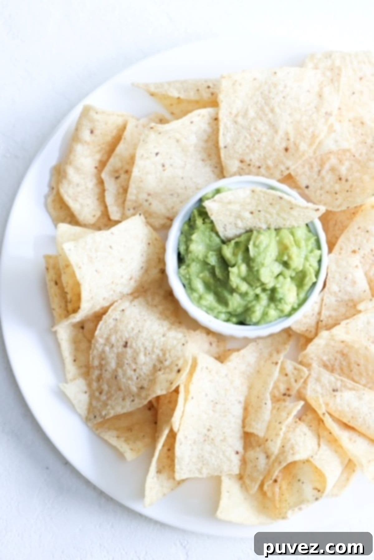 Fresh 4-ingredient guacamole served in a white bowl with crispy tortilla chips on a white plate, ready for dipping.