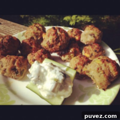 Plate of perfectly cooked Greek Meatballs garnished with fresh herbs, served with a generous dollop of tzatziki sauce.