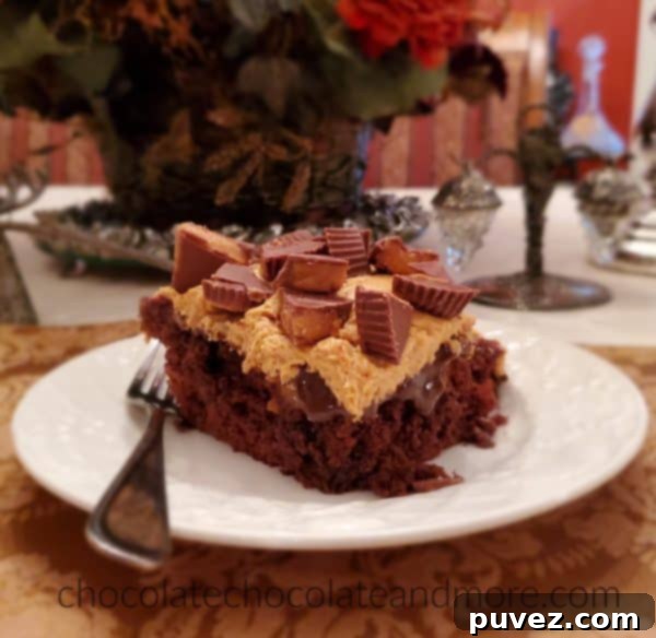 A generous slice of moist chocolate cake on a white plate, lavishly covered with creamy peanut butter frosting and topped with chopped peanut butter cups. The background is softly blurred, keeping the focus on the rich and indulgent dessert.