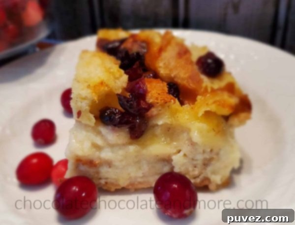 A slice of cranberry brie pudding on a white plate surrounded by fresh cranberries.