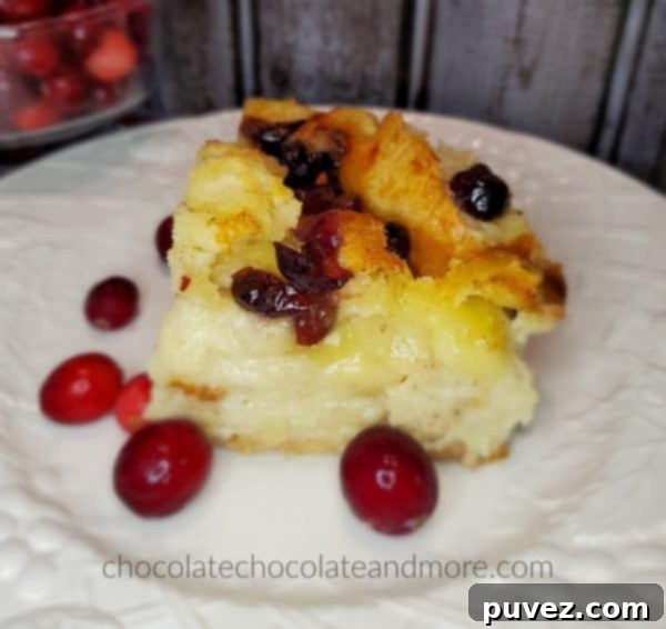 A slice of cranberry brie bread pudding on a white plate with fresh cranberries.
