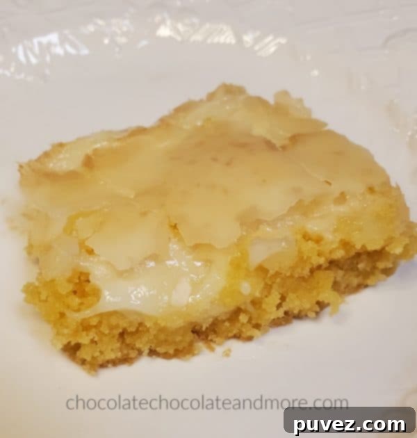 A gooey cream cheese bar on a white plate, showcasing its soft, layered texture.