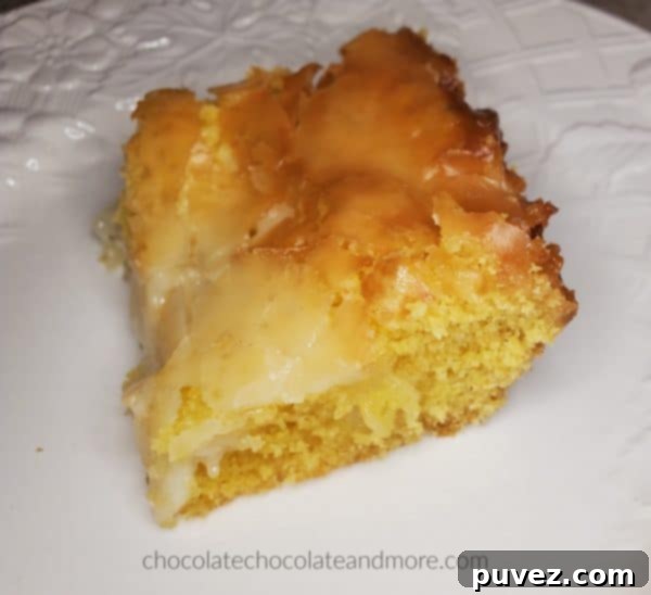 A close-up of a single gooey cream cheese bar on a white plate, showing the distinct layers of cake and creamy cheese topping.