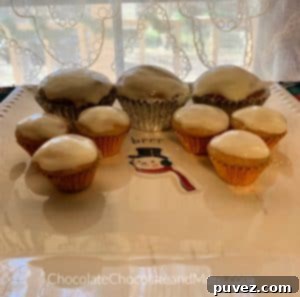 A charming plate featuring three regular-sized Eggnog Cream Cheese Cupcakes alongside six mini cupcakes, all surrounding a festive snowman figurine in the center. The backdrop of a white lace curtain adds a delicate and cozy touch to this delightful holiday dessert display.