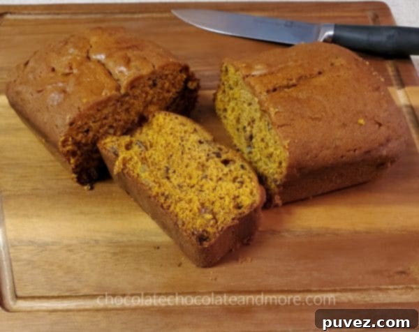 A freshly sliced loaf of homemade Pumpkin Raisin Bread on a rustic wooden cutting board with a knife, revealing its moist crumb and distribution of golden raisins and nuts.