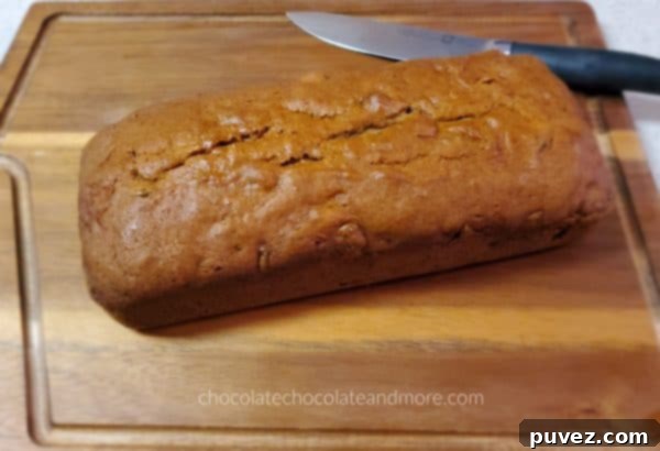 A warm, golden-brown whole loaf of Pumpkin Raisin Bread resting on a wooden cutting board with a bread knife, ready to be sliced and served.