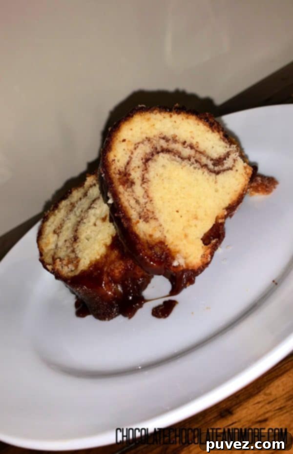 Two delectable slices of Monkey Bread Cake, showcasing their warm, gooey caramel and intricate cinnamon swirls, are presented on a white plate atop a wooden table. The inviting visual promises a delightful culinary experience.