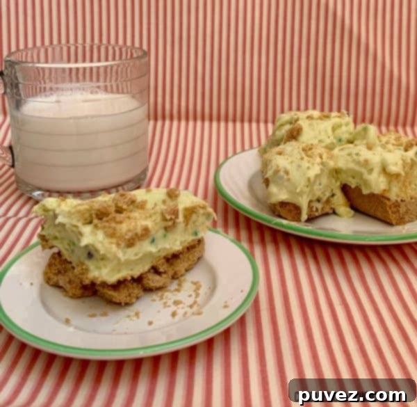 A single Birthday Cake Pudding Bar on a small white plate with a green rim, alongside a larger plate holding three more bars, and a clear glass of milk, all against a playful pink and white striped backdrop.
