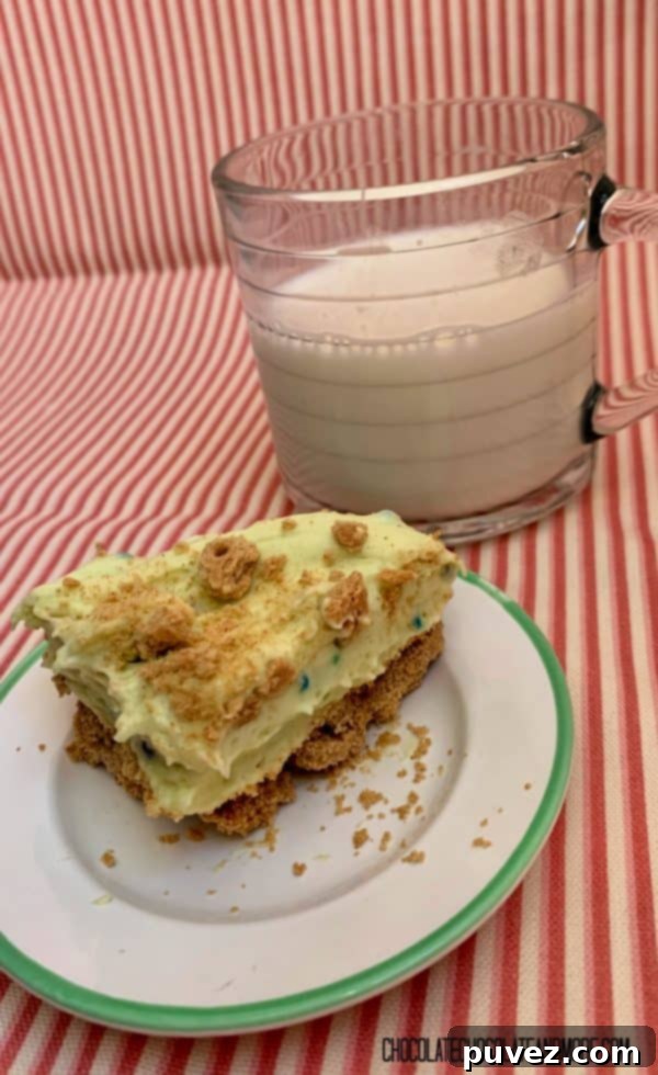 A close-up of a single Birthday Cake Pudding Bar, perfectly sliced, resting on a white plate with a green rim next to a refreshing glass of milk, highlighting its creamy layers.
