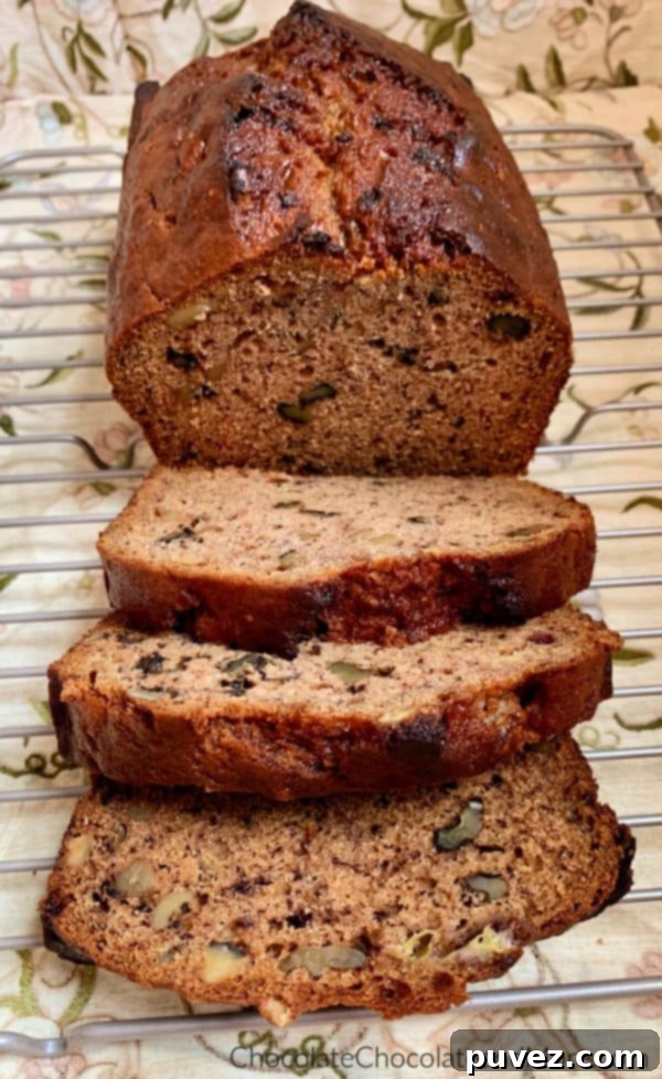 Banana nut Bread Half a loaf of Banana Nut Bread rests behind three slices on a metal cooling rack, illuminated by a warm, brown floral background, highlighting its delicious texture.