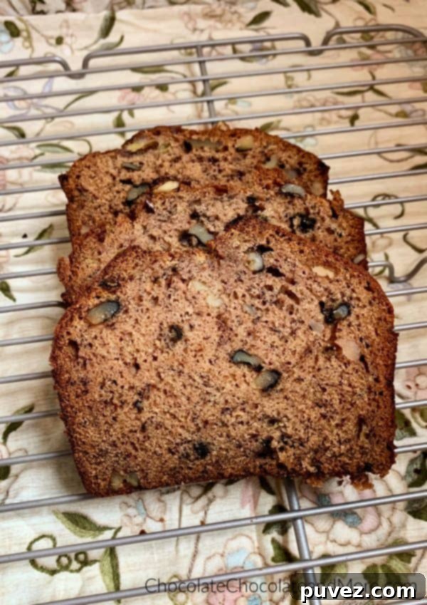 Banana Nut Bread Three golden brown slices of homemade banana nut bread are neatly arranged on a metal cooling rack, with a soft brown floral pattern in the background.