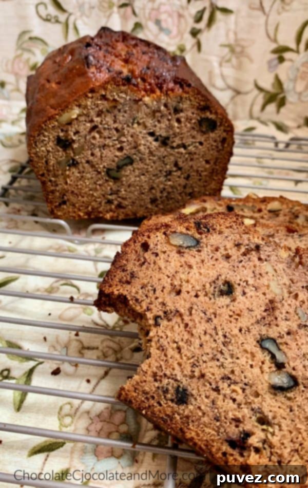 Banana Nut Bread Half a loaf of banana nut bread sits behind a single slice with a bite taken out, all resting on a metal cooling rack, inviting you to taste its homemade goodness against a soft floral background.
