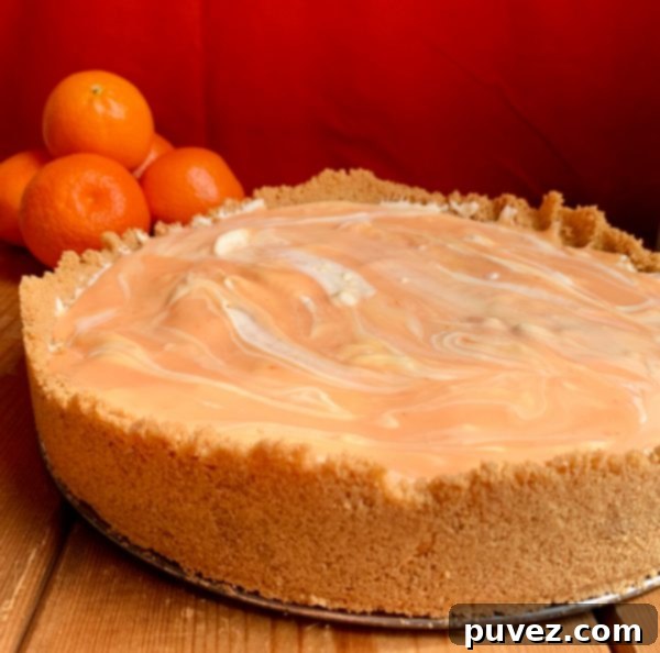 A whole Orange Creamsicle Swirl Cheesecake resting on a white cake stand in front of a warm red background, ready to be sliced and served.