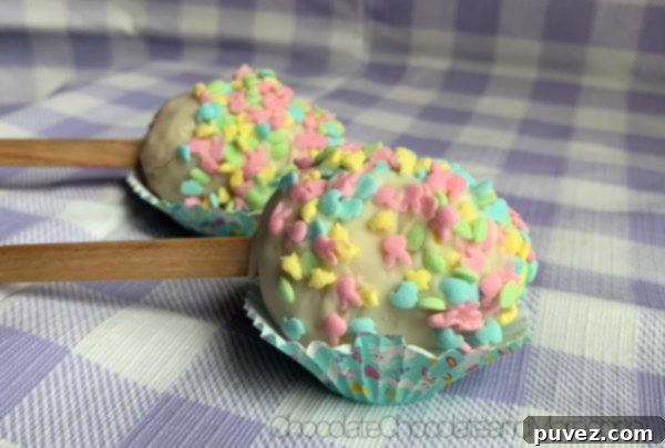 Two vibrant Easter Egg Cake Pops, nestled in mini cupcake holders, resting on a purple and white plaid background, ready for a festive celebration.
