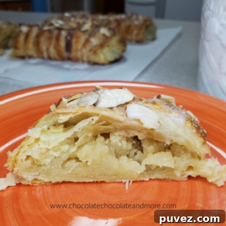 A slice of almond puff pastry on an orange plate in front of two loaves