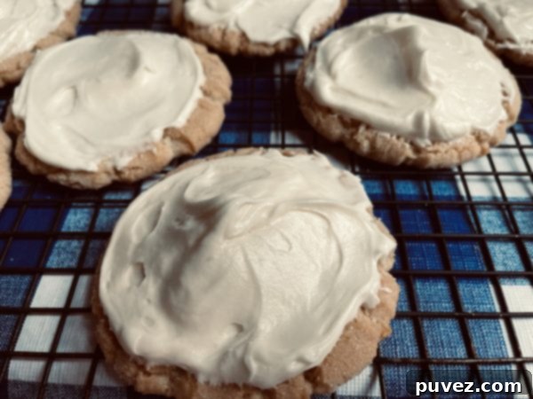 6 Cream Cheese Frosted Sugar Cookies sitting on a cooling rack on a blue and white checkered backgorund.