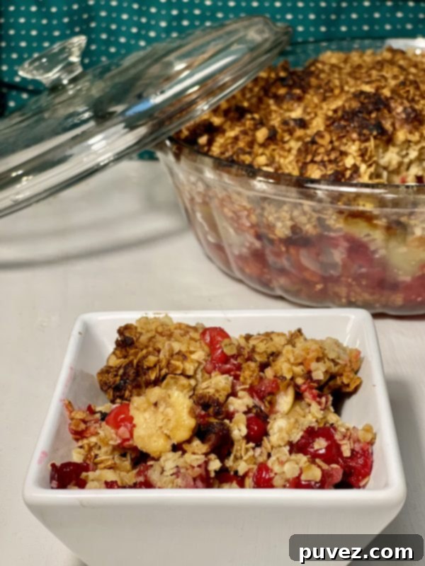 Granny's Cranberry Apple Pecan Casserole scooped into a tiny bowl with the casserole dish in the back.