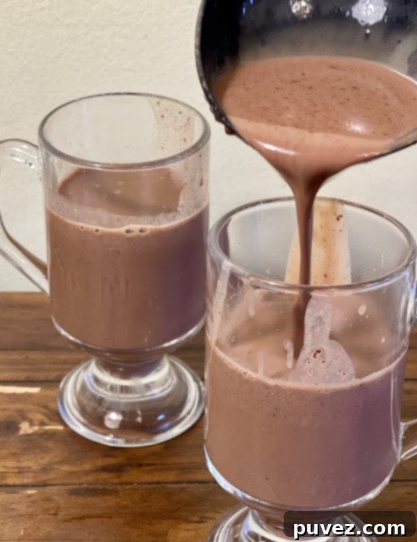Thick, creamy crockpot hot chocolate being poured into a clear mug, showing its rich texture.