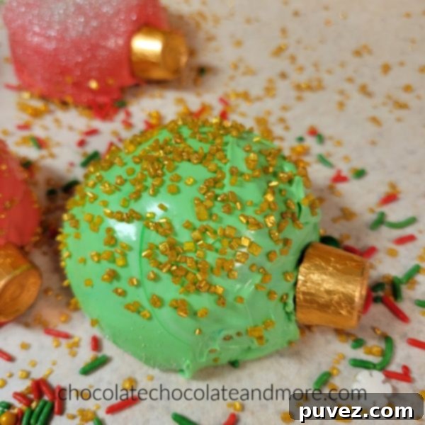 A vibrant green Christmas ornament shaped cupcake generously covered in shimmering gold sprinkles, ready for the holidays.